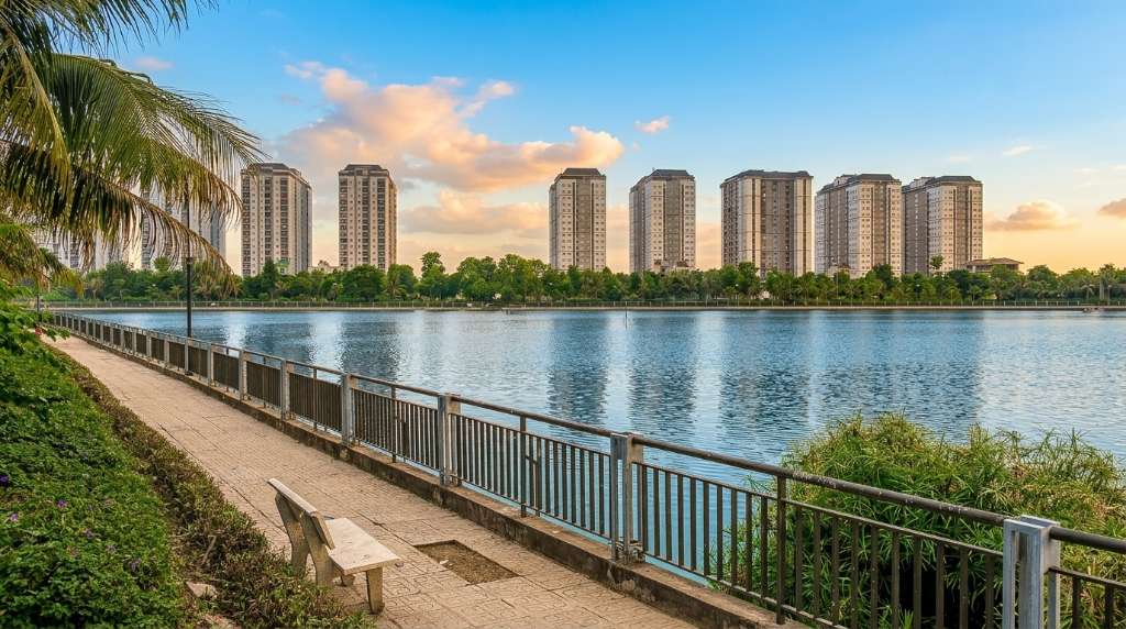 Gia đình trẻ Việt Nam gồm bố mẹ và hai con nhỏ đang đi dạo trên con đường nội khu rợp bóng cây xanh trong khu đô thị hiện đại, hai bên là hàng cây và ghế đá, ánh nắng chiều xuyên qua tán lá, bầu không khí ấm áp hạnh phúc, ảnh chụp 4K phong cách lifestyle