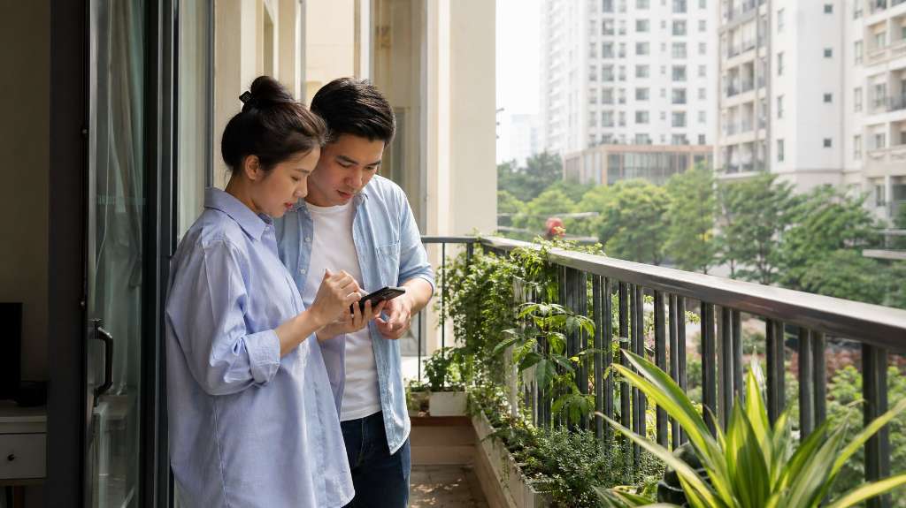 Đôi vợ chồng trẻ cùng xem điện thoại trên ban công