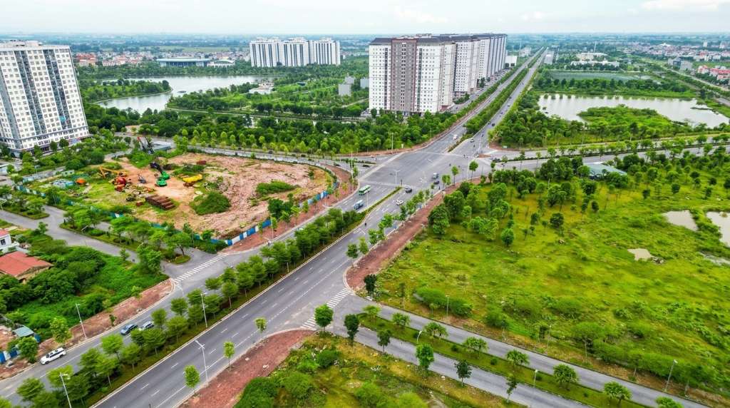 Bàn làm việc nhỏ trong căn hộ chung cư Thanh Hà 2 phòng ngủ, trên bàn có laptop mở trang bảng tính chi phí sinh hoạt, bên cạnh là cốc cà phê và chậu cây nhỏ, cửa sổ phía sau nhìn ra view các tòa chung cư và cây xanh bên dưới, ánh sáng tự nhiên ban ngày chiếu vào, không gian gọn gàng ấm cúng, góc chụp 45 độ từ trên xuống