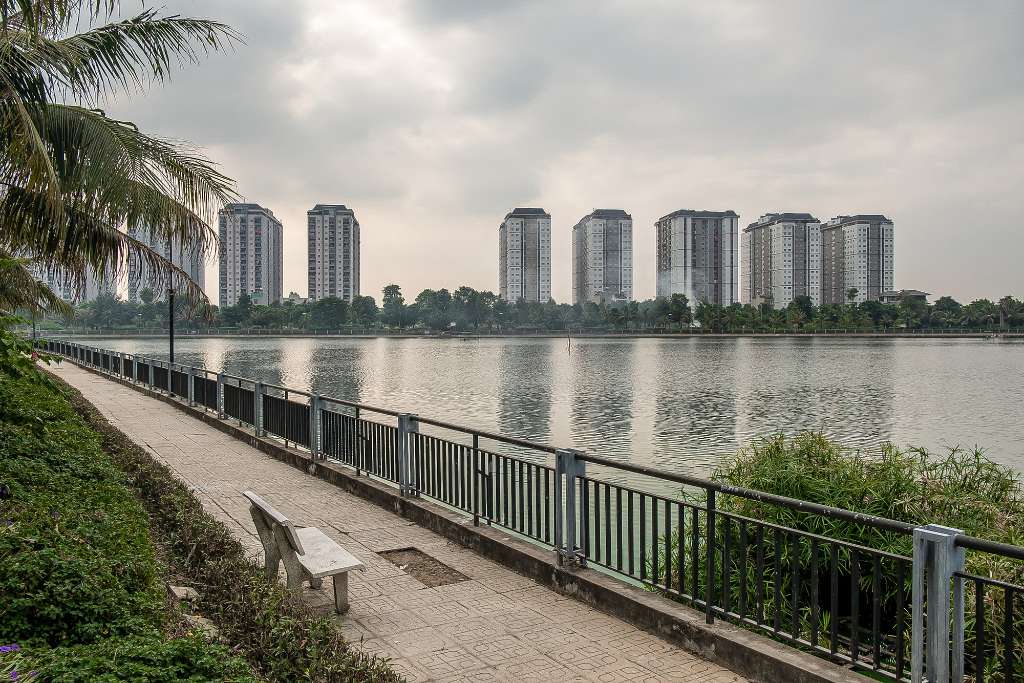 Ảnh chụp góc rộng điểm dừng xe buýt có mái che trong khu đô thị Thanh Hà, bên cạnh là vỉa hè lát gạch sạch sẽ, phía sau là tòa chung cư HH cao tầng, có vài cư dân đang đứng chờ xe, ánh sáng ban ngày tự nhiên, góc chụp ngang tầm mắt